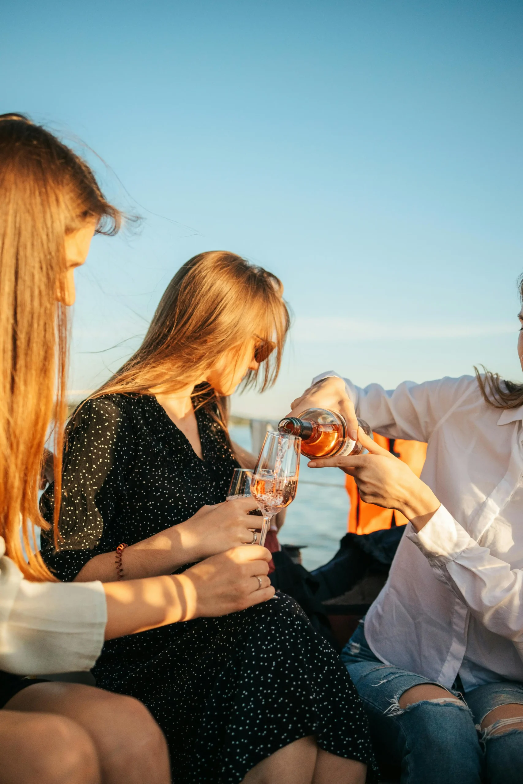 Three women enjoying champagne on a yacht at sunset, showcasing friendship and leisure.